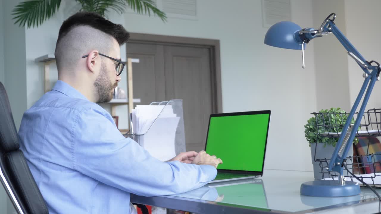 joven caucásico usando una pantalla verde de portátil en el escritorio de casa.