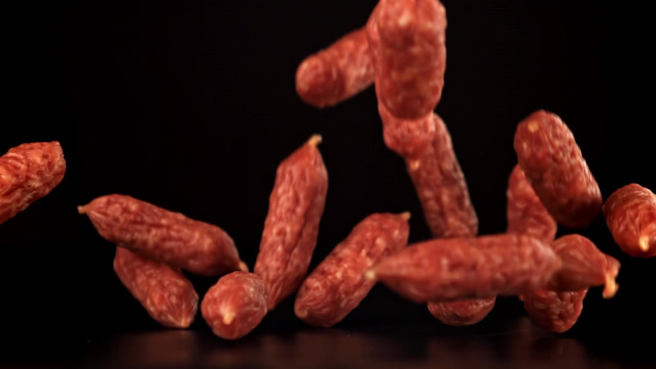 Mini salsicce di salame che cadono al rallentatore su sfondo nero.