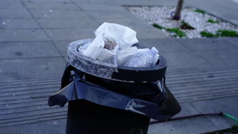 filled black rubbish bin with black plastic bag and litter