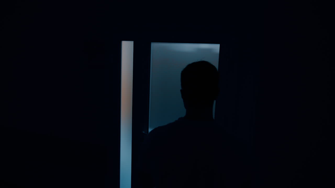 Male silhouette moving in the dark room in front of light door. Man worries while his wife is delivering a baby. Top view.