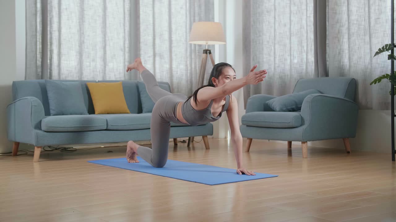 スポーツ服を着た若いアジア人アスリート女性が自宅のマットの上でバランステーブルポーズでヨガをしています