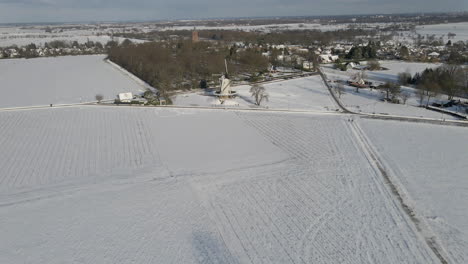 Descripción-Aérea-Del-Hermoso-Paisaje-Rural-Cubierto-De-Nieve-Con-Un-Molino-De-Viento-Tradicional-En-El-Borde-De-Un-Pequeño-Pueblo