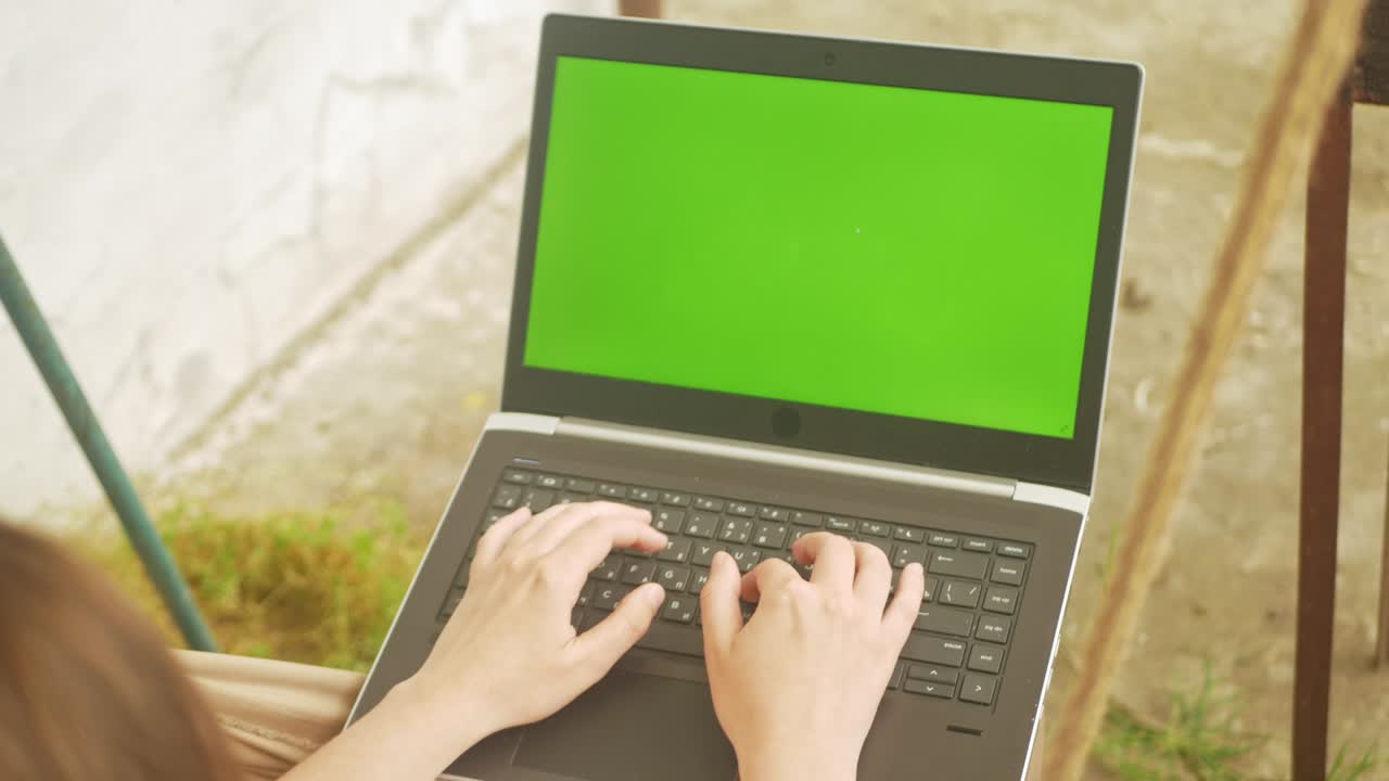 woman rides on a swing and communicates with friends using a laptop. Green screen, rest in the yard of the house. Outsdoor. Social networks, the Internet, messages. In nature. fingers on the keyboard