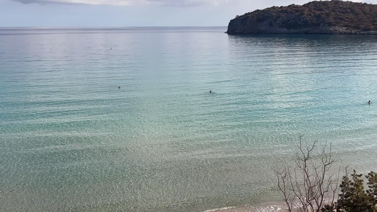 Calm and transparent waters at Voulisma Beach with a rocky hill in the background, Crete Greece