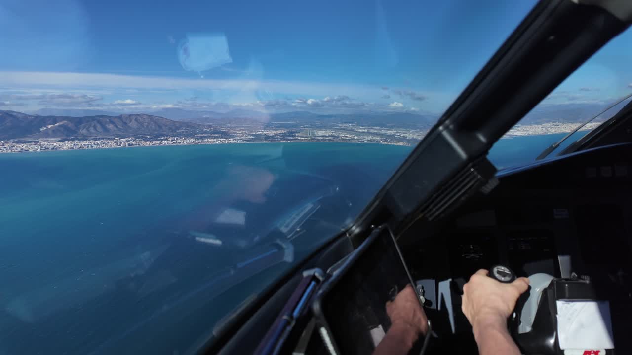 Tampilan imersif dari sudut pandang pilot di dalam pesawat jet dalam pendekatan terakhir ke bandara Malaga (AGP), dengan pemandangan tangan pilot yang menggenggam yoke, dan landasan pacu pantai di depan