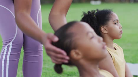 Mixed-race-female-teacher-correcting-diverse-group-of-schoolchildren-while-yoga-stretching-outdoors