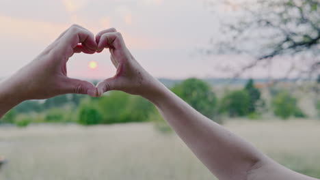 hands form a symbolic love heart symbol against the romantic setting sun