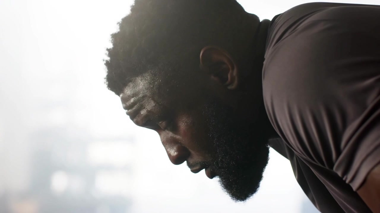 Athletic man breathing deep, lifting head and regaining focus by backlit gym window, sweat showing