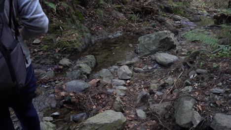 Male-hiker-walking-down-to-small-brook-inside-dark-forest-area