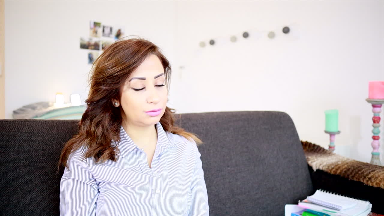Middle Eastern Woman Sitting And Relaxing On Sofa While Drinking Hot Coffee In Morning. - tilt up