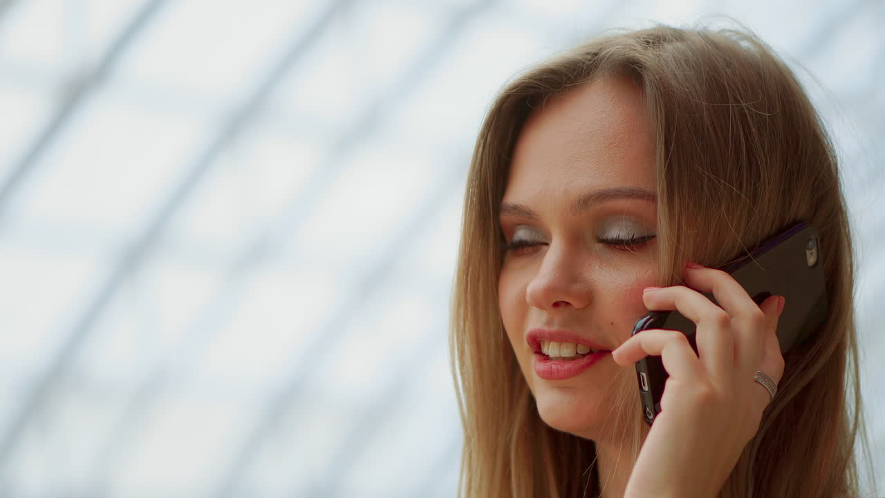 아름다운 소녀가 스마트폰으로 이야기하고 쇼핑백과 함께 쇼핑몰에 앉아 있습니다