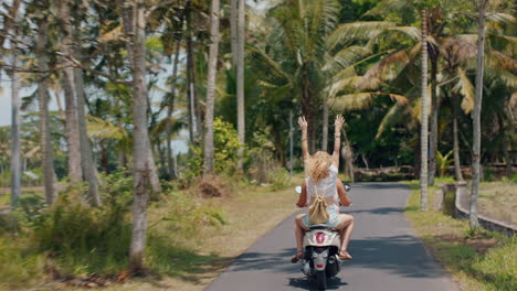 travel couple riding motorbike on tropical island happy woman celebrating freedom with arms raised enjoying vacation road trip with boyfriend on motorcycle ride rear view