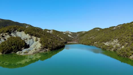 lake with calm water surface on high mountains with trees forest reflecting bright blue sky, sunny day