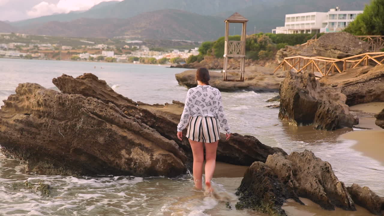 White brunette walking barefoot on a rocky beach in Greece.