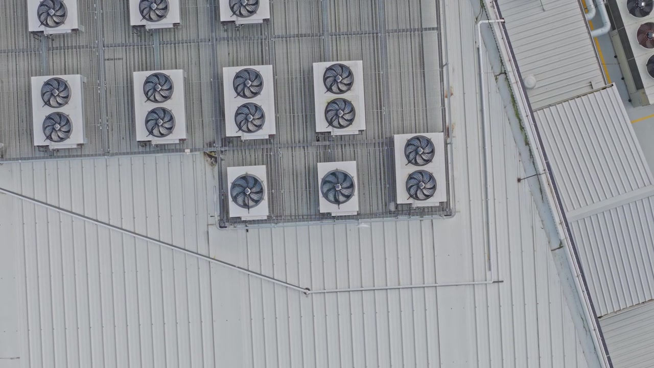 Drone shot captures a high-tech data centre rooftop filled with large HVAC systems, cooling fans, and metallic vents under soft daylight, highlighting industrial infrastructure in clear detail.