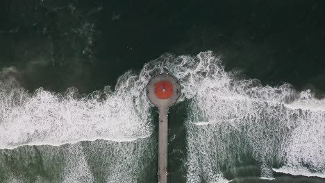 view of a pier with a roundhouse aquarium and visitors in a beautiful sea with waves and a distant view straight down, manhattan