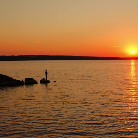 people fishing at sunset. beautiful orange sun on the evening sky. silhouette fisherman with fishing rod catching fish on the stone in water. men relax near the water.
