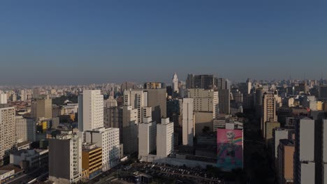 aerial view of são paulo's dense skyline under a clear blue sky, with the são paulo state flag prominently displayed. high-rise buildings showcase the city's urban density and modern architecture
