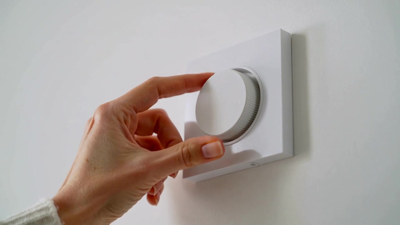 Reaching right hand manicured nails knit-sleeve turning wall dial at home, adjusting thermostat