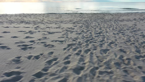 AERIAL:-Pan-Shot-of-Sandy-Beach-Filled-with-Foot-Prints-and-Human-Tracks-with-Sea-Visible-in-the-Background