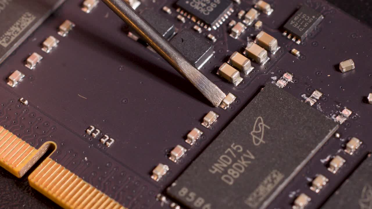 Close-up of metal tool examining microchip components on circuit board under controlled studio lighting