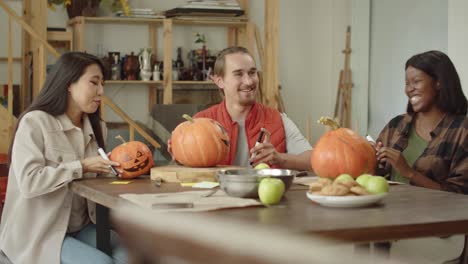 friends are sitting at the table and talking about their painted halloween pumpkins