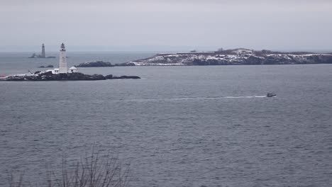 a law enforcement vessel battles the waves off the coast of hull, passing in front of boston light