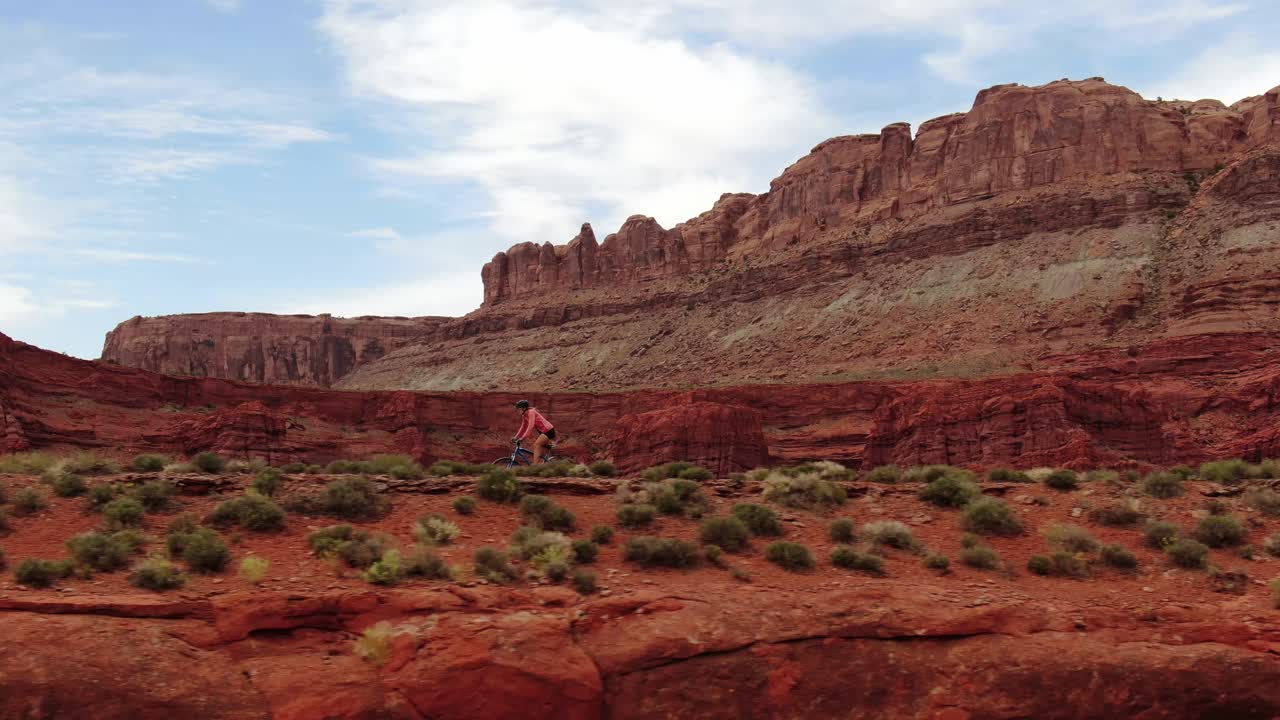 Ripresa aerea in movimento laterale a sinistra di donna in mountain bike nel deserto di arenaria di Moab