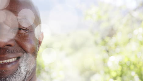 Animation-of-spots-of-light-over-smiling-african-american-man-with-copy-space-on-nature-background