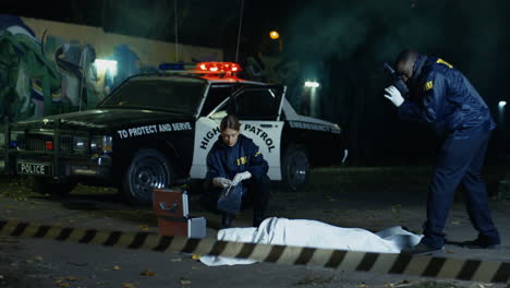 young woman police investigator sitting at the dead body on the ground and picking evidences