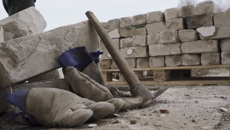 guantes y pico en el sitio de construcción mientras el trabajador camina en segundo plano