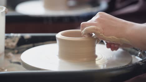 female potter makes a pot on the pottery wheel close-up