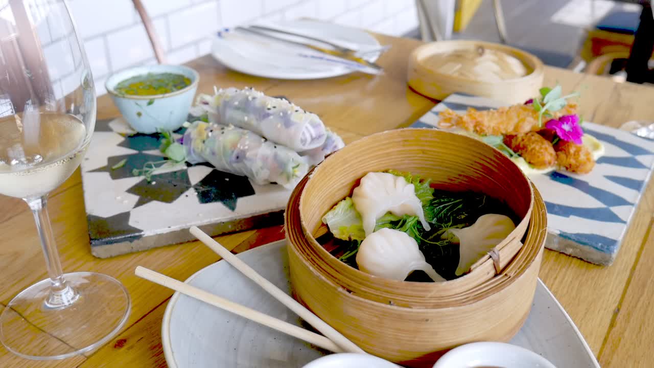Dim sum in bamboo steamer with other Asian cuisine plated on tabletop, closeup