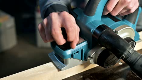 Close-up of a carpenter's hand working with an electric plane in a home workshop