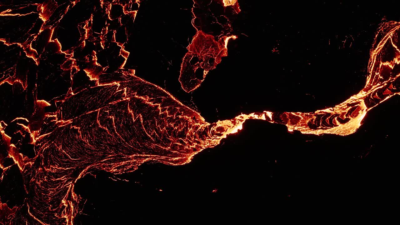 Lava fusa scorre attraverso roccia scura, con la superficie che si solidifica e si spacca, vista dall'alto.
