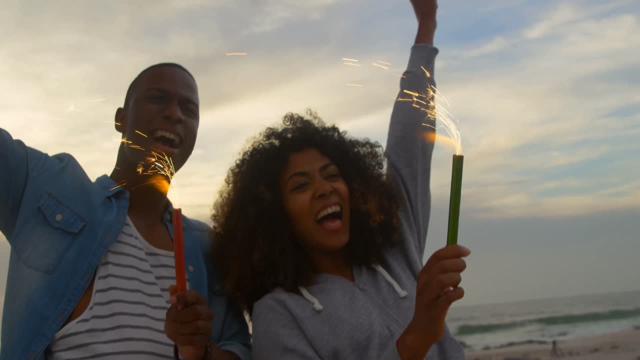 Low angle view of African american couple holding sparklers in hand at beach 4k