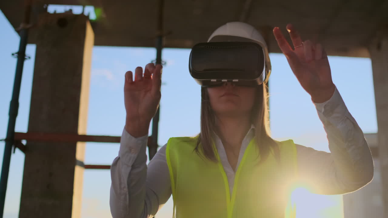 una mujer ingeniera en un sitio de construcción en gafas de realidad virtual mueve sus manos simulando el trabajo de la interfaz del futuro al atardecer