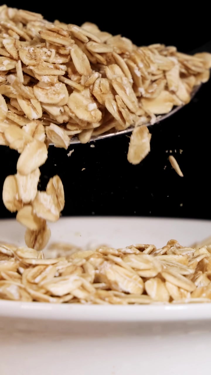 Un cucchiaio fa cadere cereali di mais tostati in una ciotola, creando uno schizzo dinamico su sfondo nero