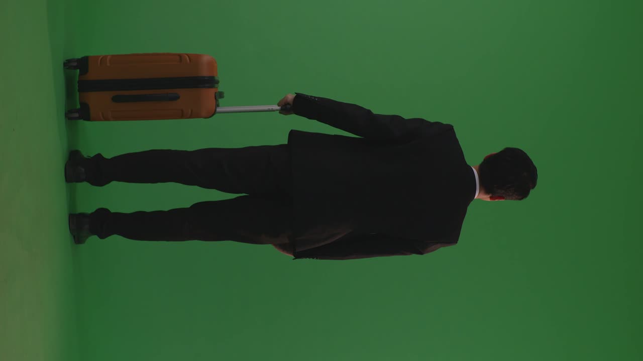 азиатский бизнесмен-путешественник с багажем, идущий и стоящий на зеленом экране в фоновой студии во время захода солнца.