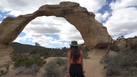 Young-Female-Photographer-Approaching-to-Natural-Sandstone-Arch,-Shiprock-Navajo-Territory,-New-Mexico-USA,-Full-Frame-Slow-Motion