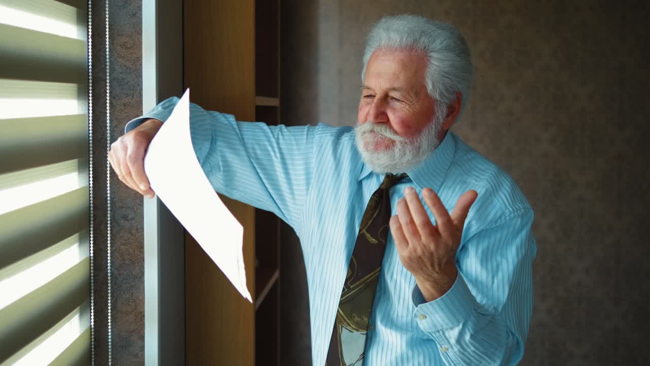 el anciano enojado se molesta leyendo un documento de malas noticias a la compañía. el dueño de la compañía está de pie junto a la ventana en la oficina y está molesto por los malos resultados comerciales