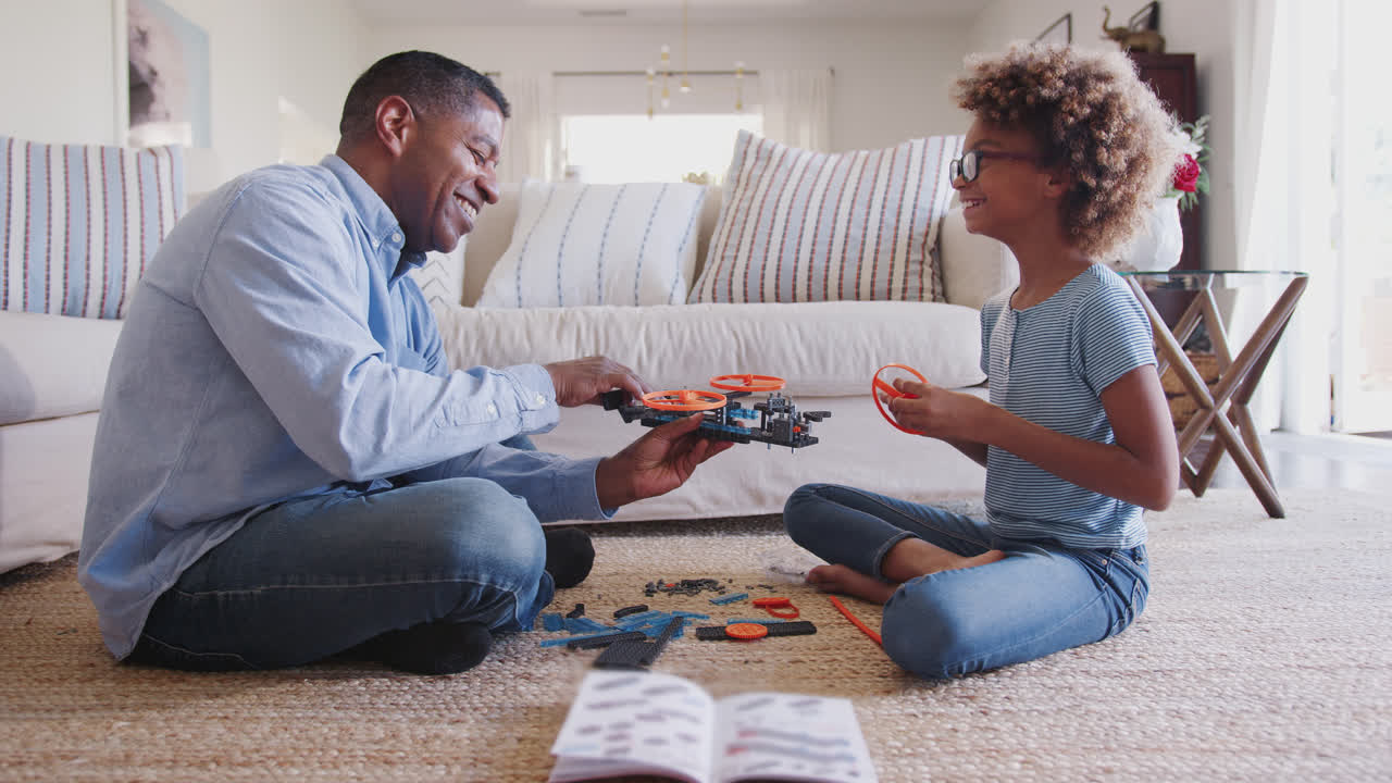 Pre-teen girl and grandad sitting on the floor constructing a toy, looking at each other, side view