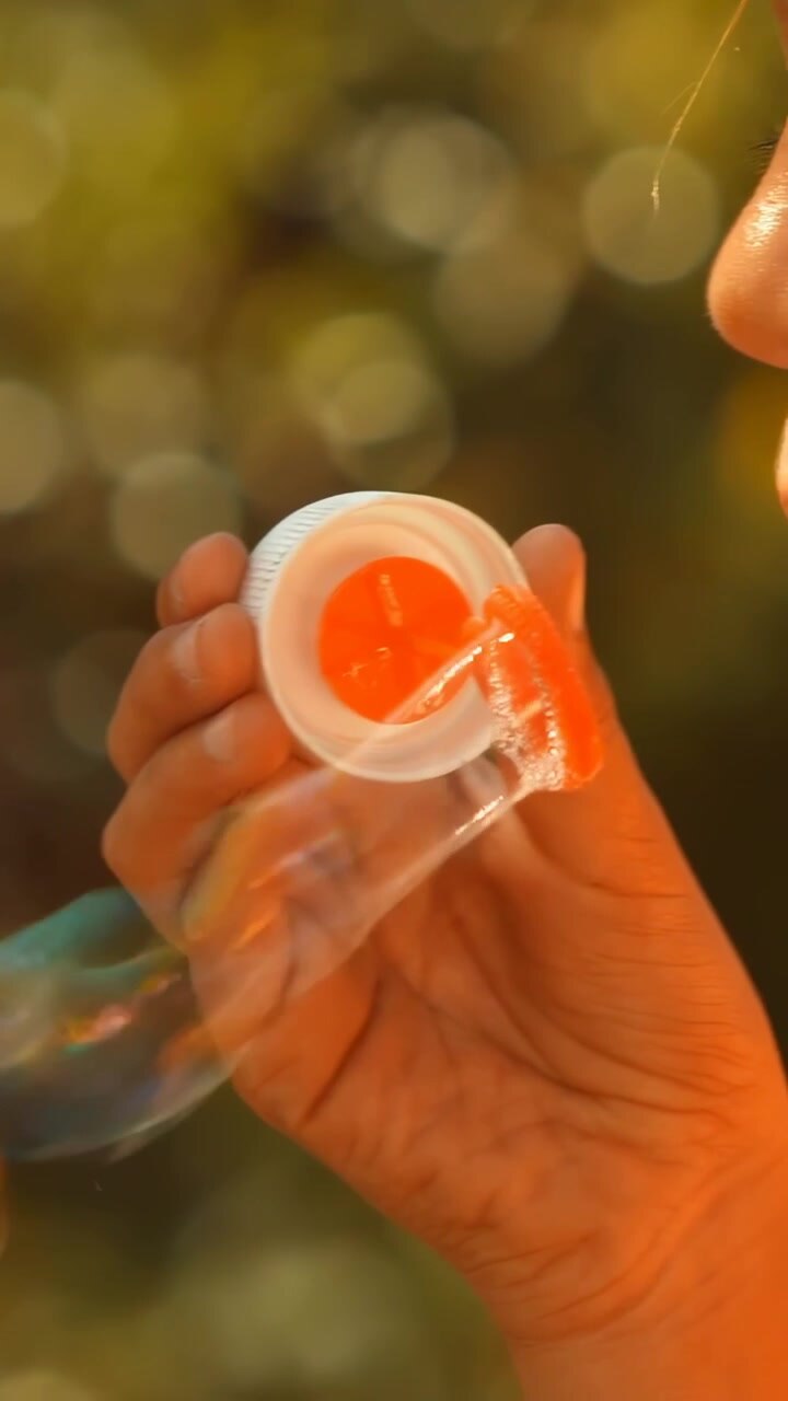 Vertical video: Opening cap on yellow bottle, kid in blue tee dipping wand, making bubbles in park
