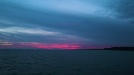 dark blue hour with pink gradient on horizon above water, aerial push in