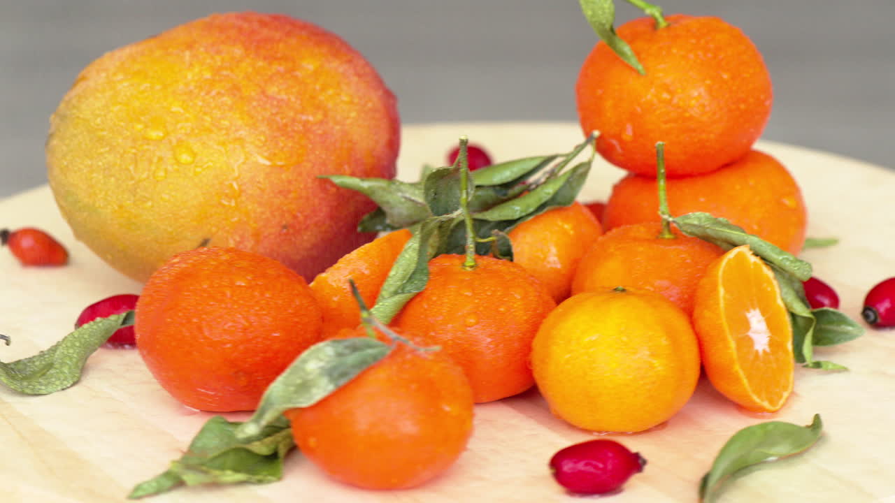 Composition with sliced rotating oranges, mango, rosehip and green leaves, close up with water drops
