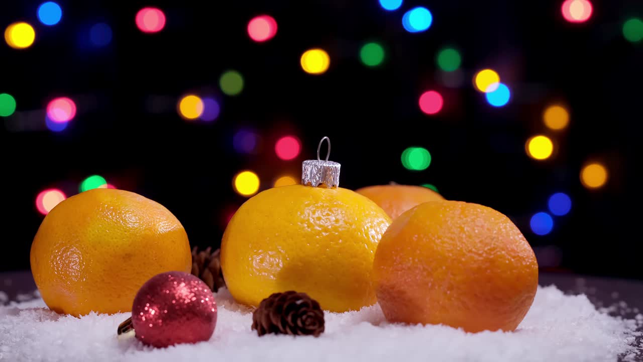 4k. frutas de tangerina naranja de navidad y juguetes de pelota roja en la rotación de la nieve. guirnalda de navidad parpadeante. decoración de año nuevo.