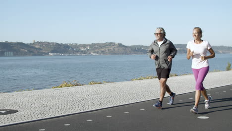 active man and woman jogging on asphalt road along sea