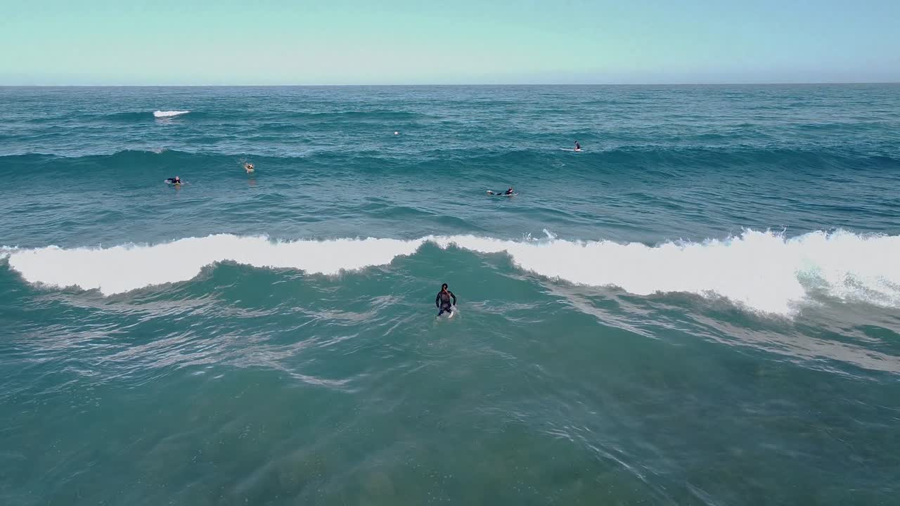 Wide aerial view of a group of surfers paddling out to sea and surfing small waves
