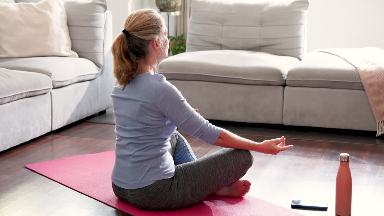 Senior woman meditating on yoga mat at home, finding inner peace