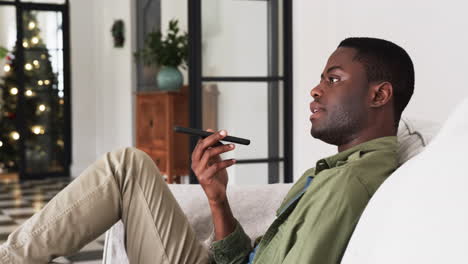 relaxing at home, man using smartphone voice assistant near christmas tree